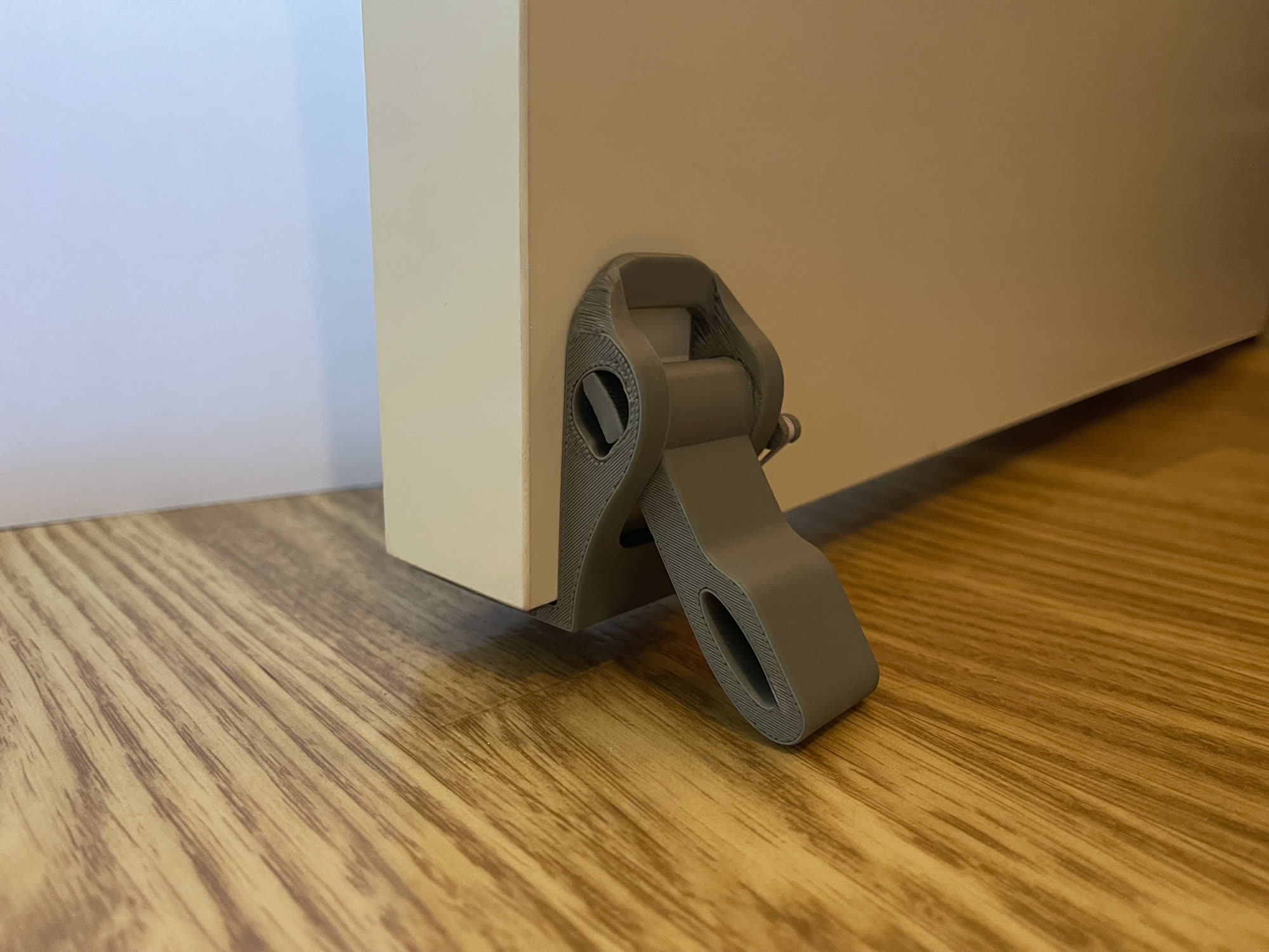 3D-printed HOLD prototype clamped on a door, arm deployed against the floor